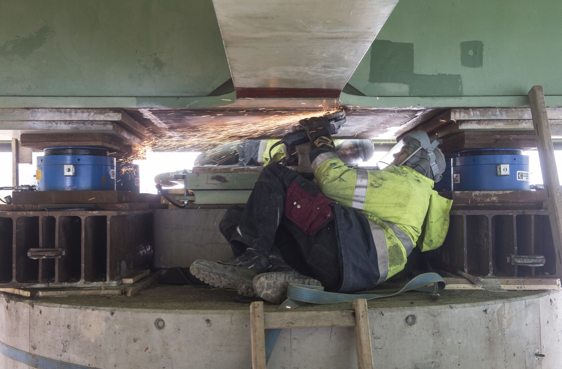 Instandhaltungsarbeiten am Brückentragwerk an der U6-Brücke zwischen Handelskai und Neue Donau. Mitarbeiter schleifen die entfernten Schweißnähte des alten Tragwerks glatt. Blaue Hydraulikpressen heben die Brücke an.