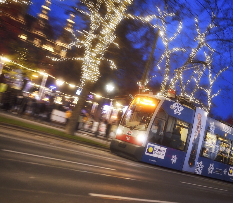 Fahrzeuge der Wiener Linien im weihnachtlich beleuchteten Wien. Hier eine Straßenbahn vor dem Rathausplatz.