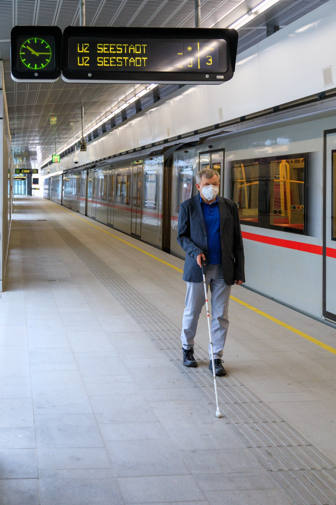 Ein blinder Fahrgast bewegt sich mit einem Langstock auf dem taktilen Leitsystem einer U-Bahn-Station.