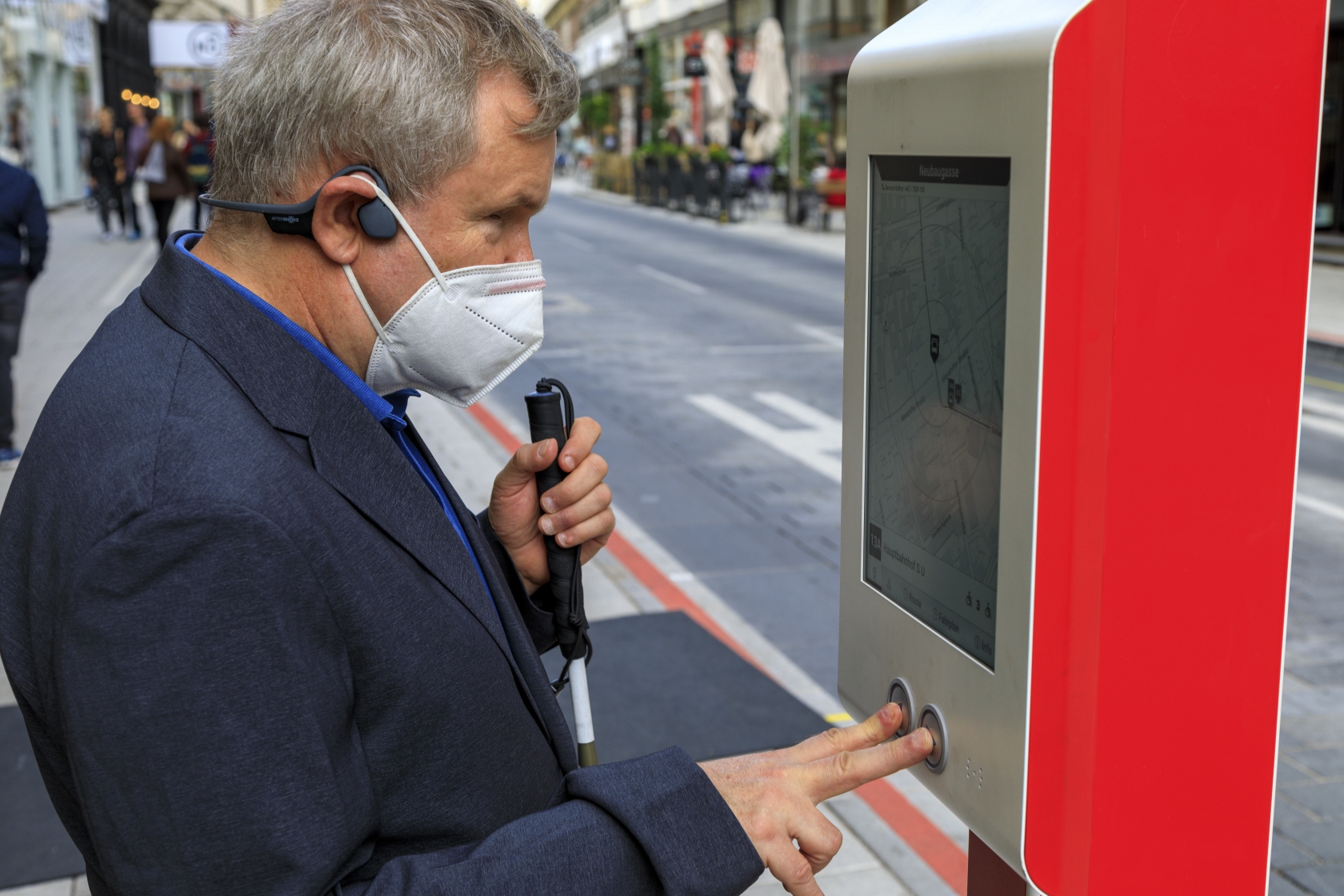 Ein blinder Mann benutzt das sogenannte E-Paper einer digitalen Infosäule an einer Bushaltestelle.