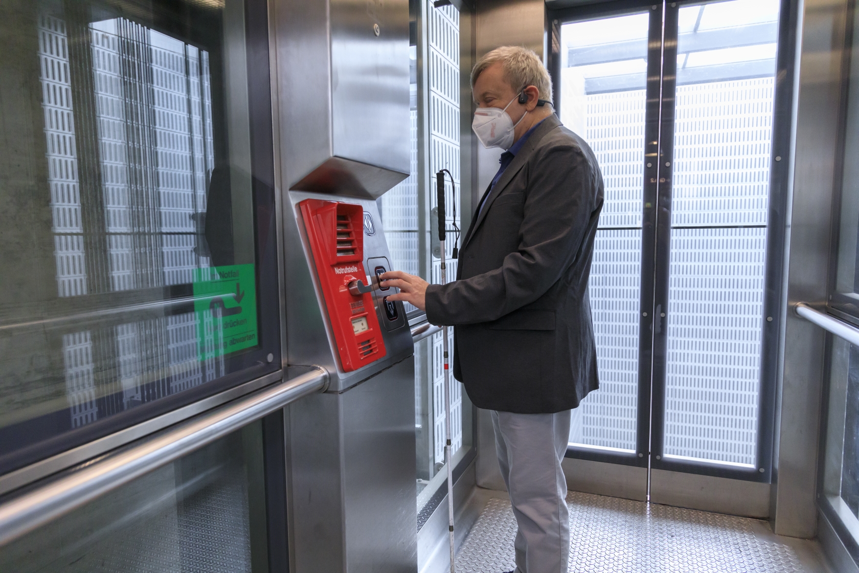 Ein blinder Mann in einem Lift. Er benutzt die taktilen Druckknöpfe.